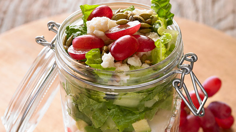 Glass Jar filled with layers of lettuce, grape and cheese.