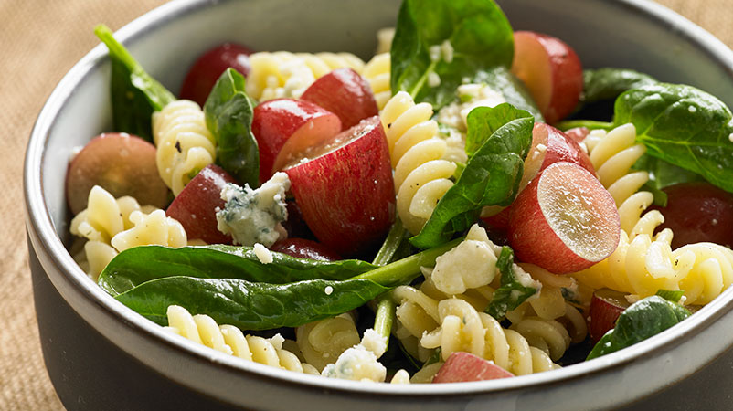 Pasta salad in bowl with rotini, red grapes and spinach