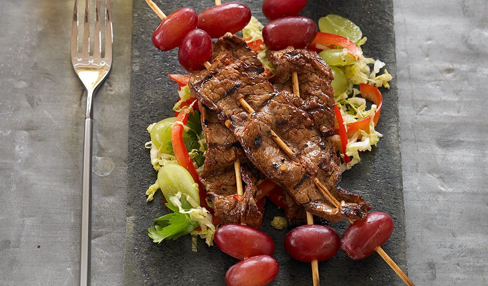 korean barbecue flank steak skewered with red grapes over lettuce on slate plate with champagne