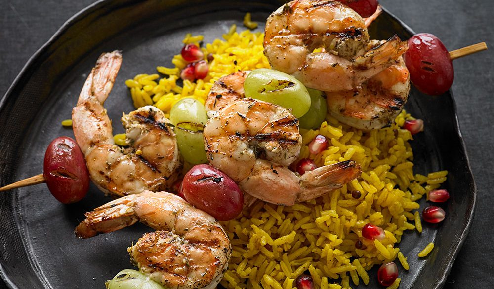 shrimp and green grapes on skewers with yellow rice on cast iron skillet